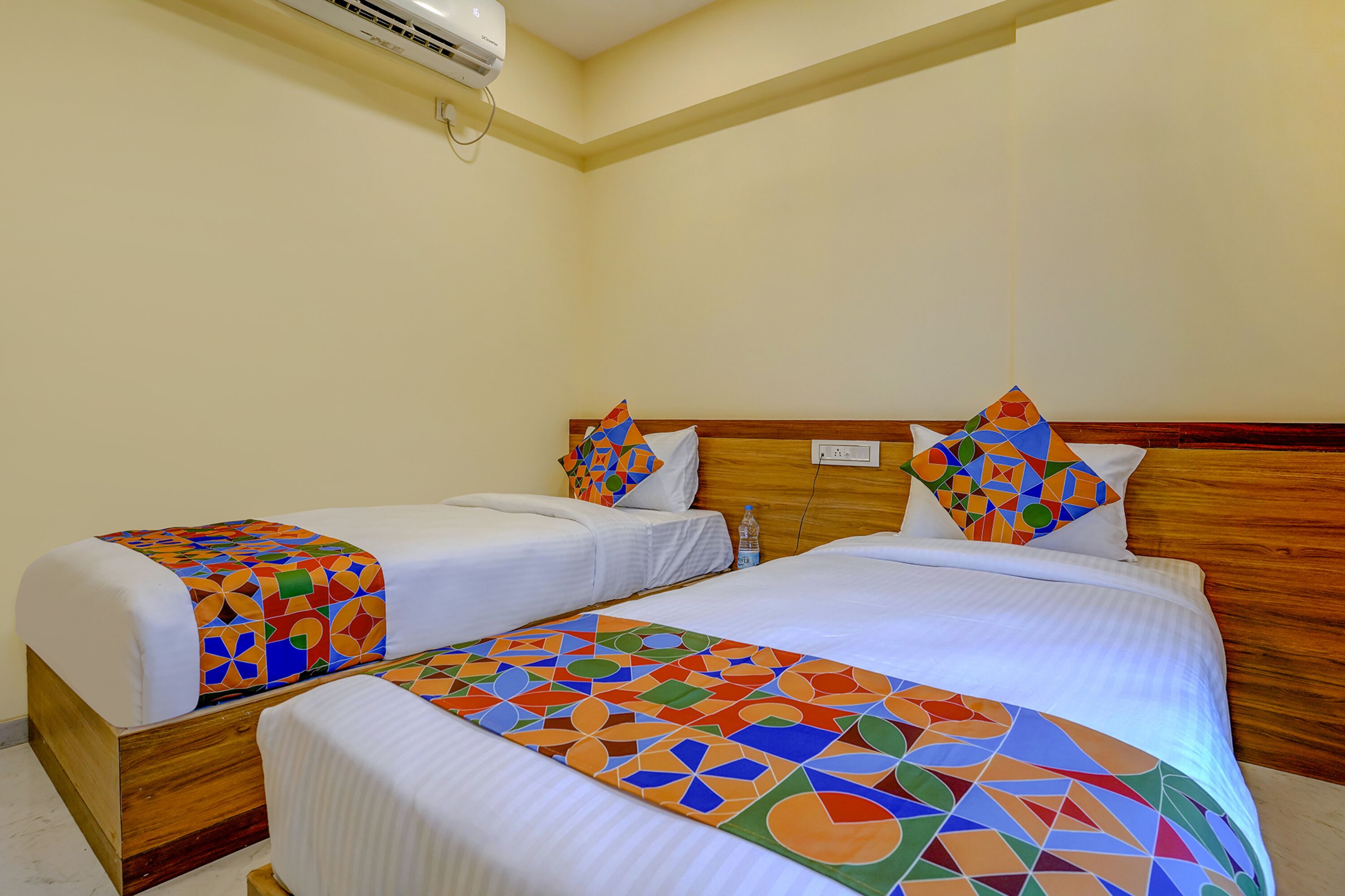 Quarto de hotel com duas camas, cada uma com colcha e almofadas de padrão geométrico colorido.