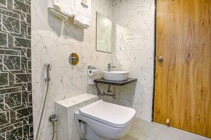 Un baño con inodoro blanco, un lavabo con espejo y ducha con cabezal de ducha de mano.