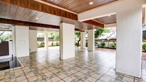 A spacious indoor area with a tiled floor and wooden ceiling beams, featuring large pillars and a view of the outdoors. - Fabhotel Crystal Homes (Pune)