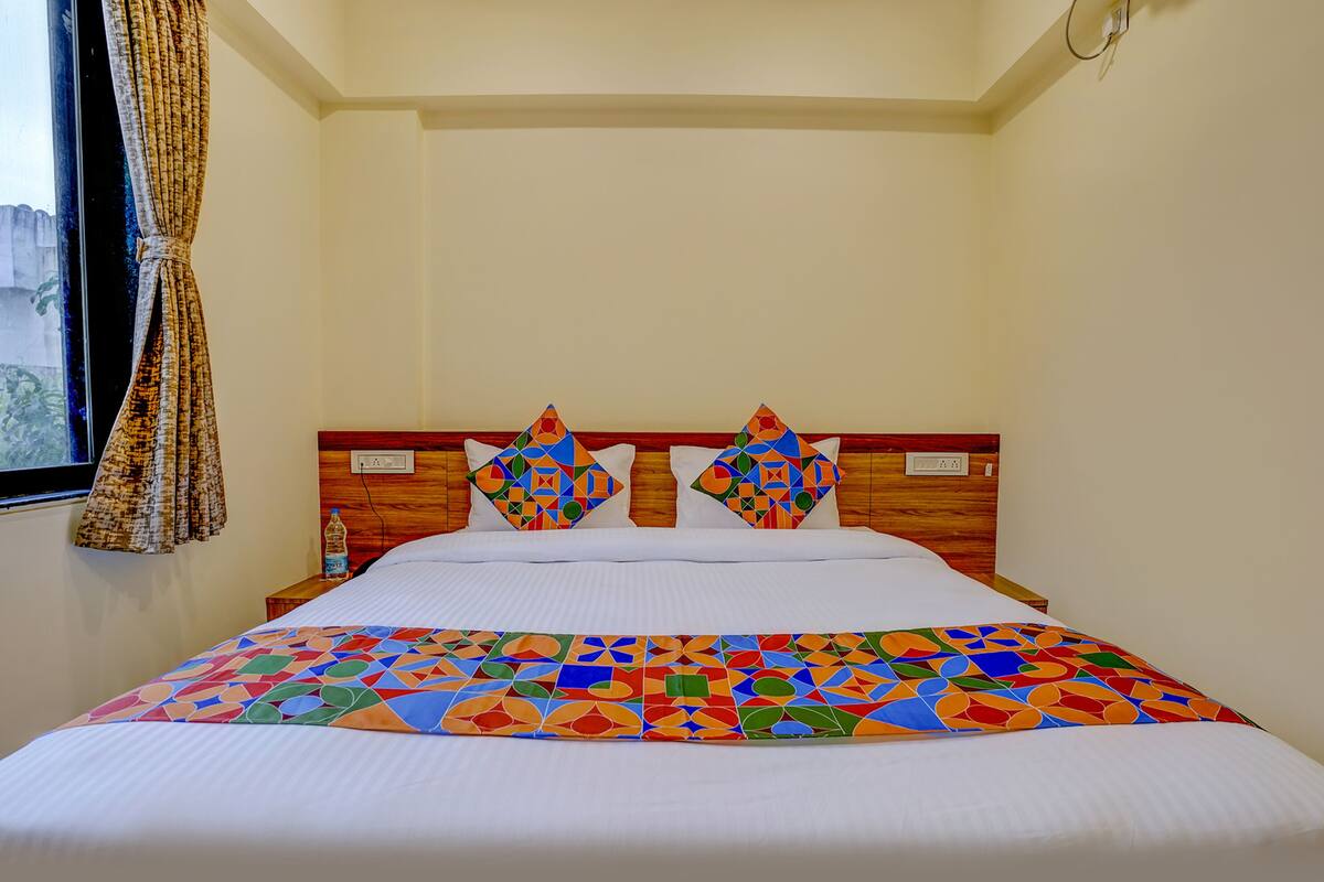 A hotel room with a bed, a wooden headboard, and a window with curtains.