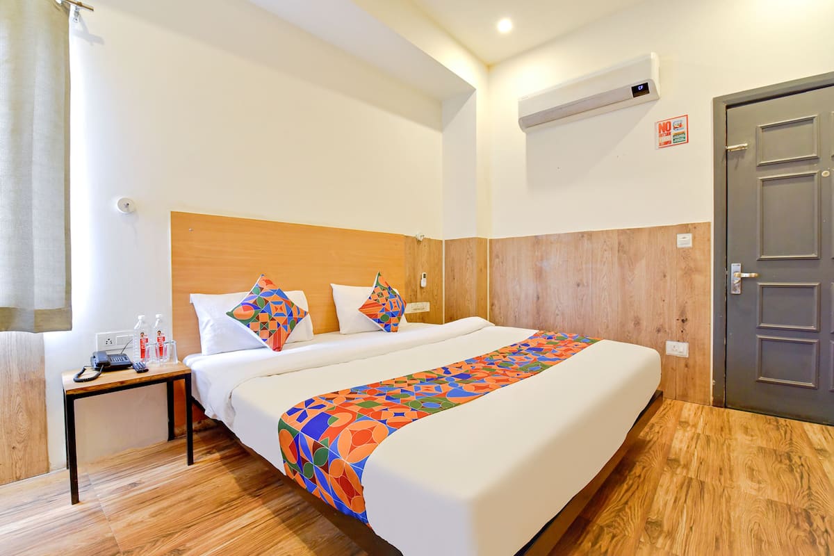 A hotel room with a large bed, wooden headboard, and a bedside table with a phone and toiletries.