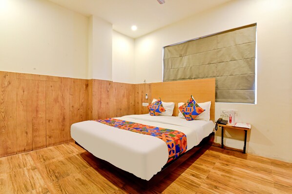 Habitación de hotel con pared de paneles de madera, una cama grande con una colcha colorida, una mesita de noche con un teléfono y una ventana con vistas.