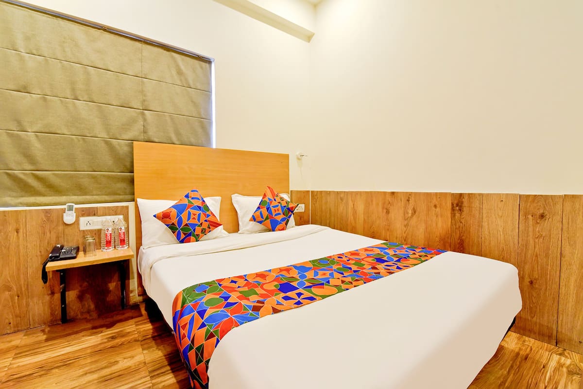 A hotel room with a wooden headboard, a bedside table with a phone and bottles, and a colorful geometric-patterned bedspread.