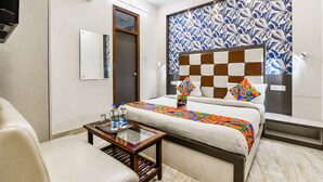 Une chambre d’hôtel avec un lit, une table de chevet avec des bouteilles d’eau, une chaise, un climatiseur fixé au mur et une tête de lit à motifs.