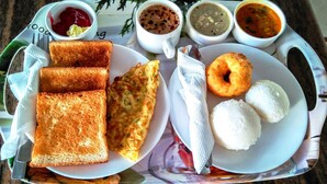 Un plateau avec des toasts, un œuf au plat, du riz blanc, un beignet et diverses sauces.