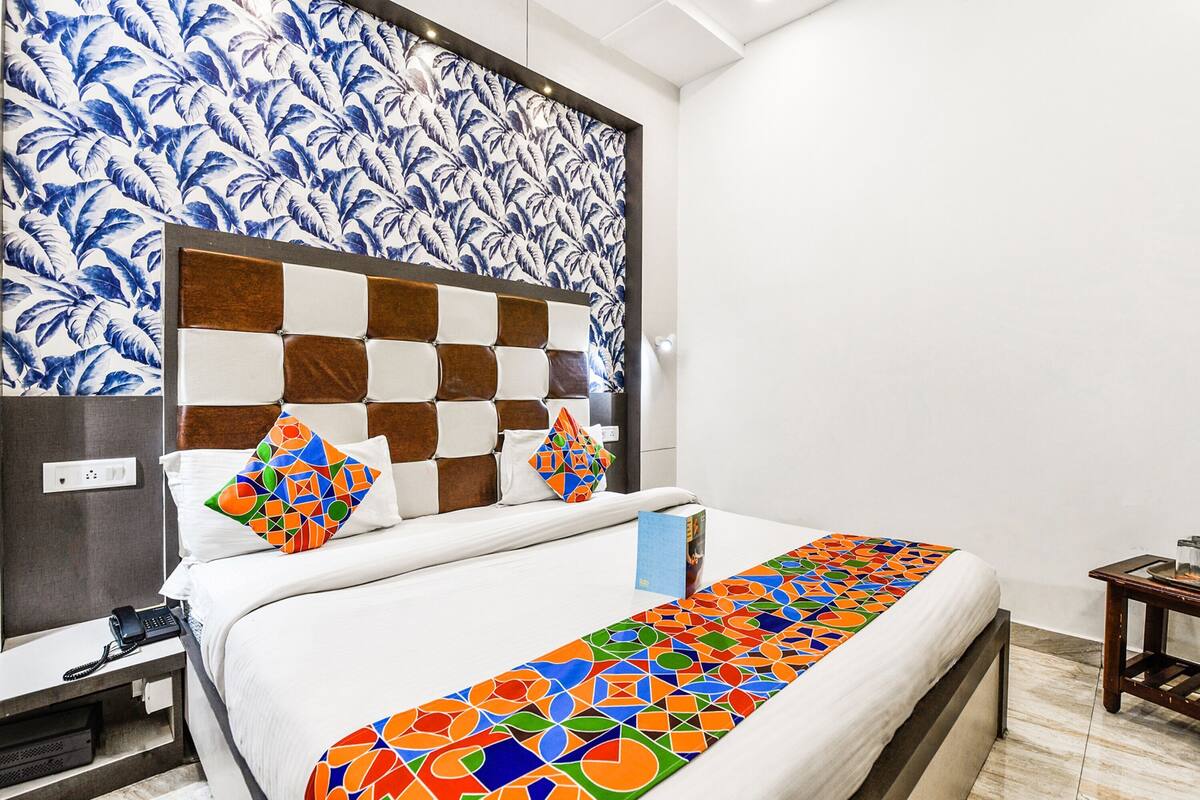 A hotel room with a bed, a nightstand, a telephone, a wall with a blue and white pattern, and a checkered headboard.