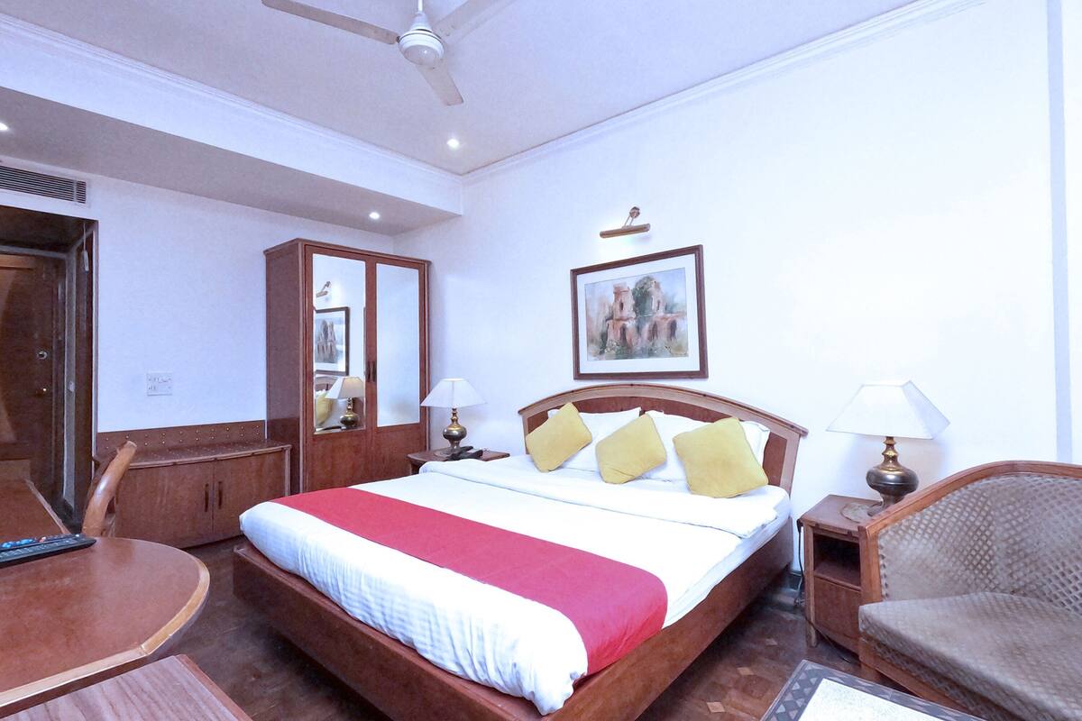 A hotel room with a bed, bedside tables, a chair, a desk, and a ceiling fan.