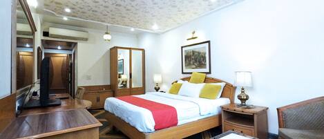 A hotel room with a wooden bed, bedside tables, a desk, a chair, a mirror, and a ceiling with floral patterns.