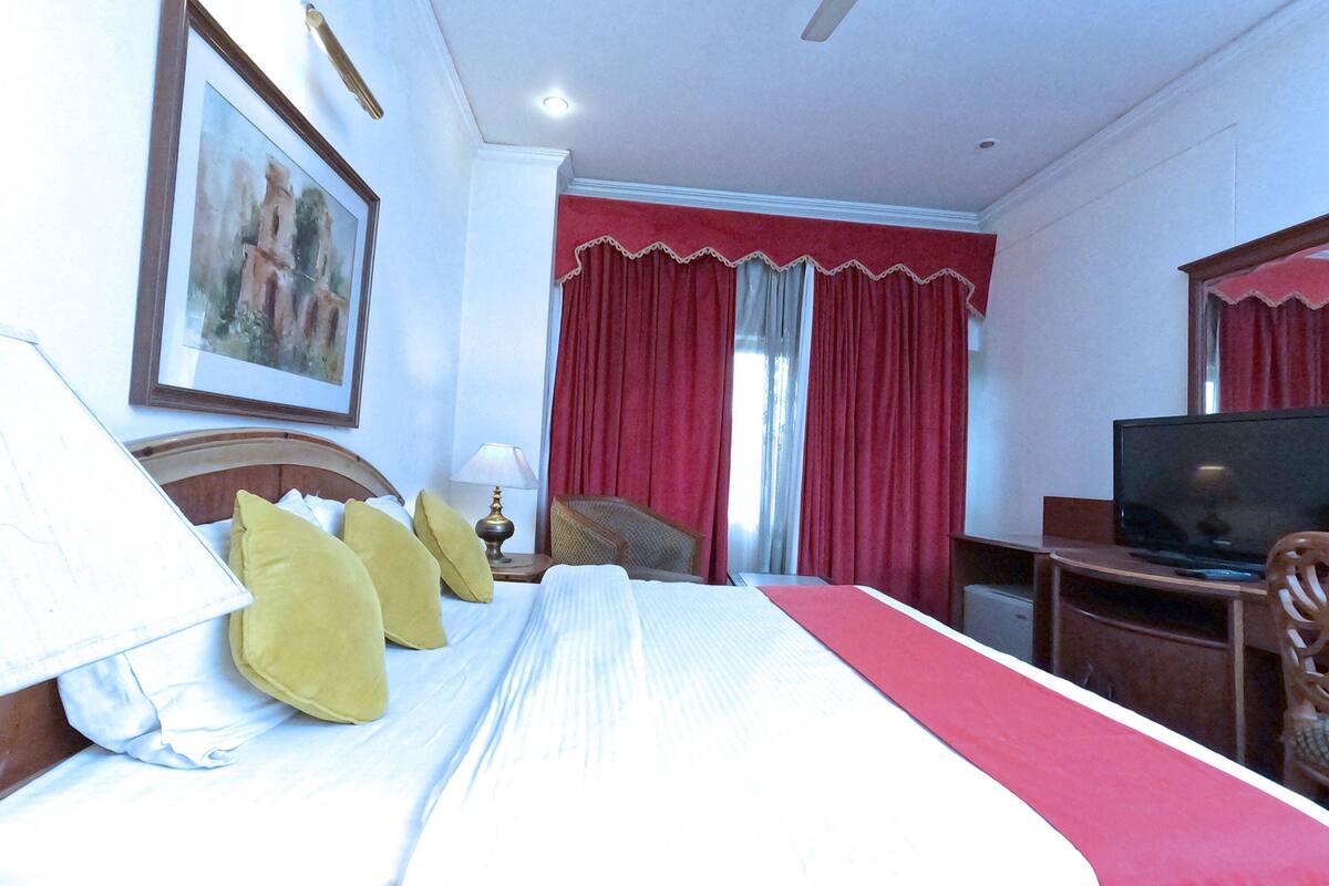 A hotel room with a bed, pillows, a television, a desk, and a chair.