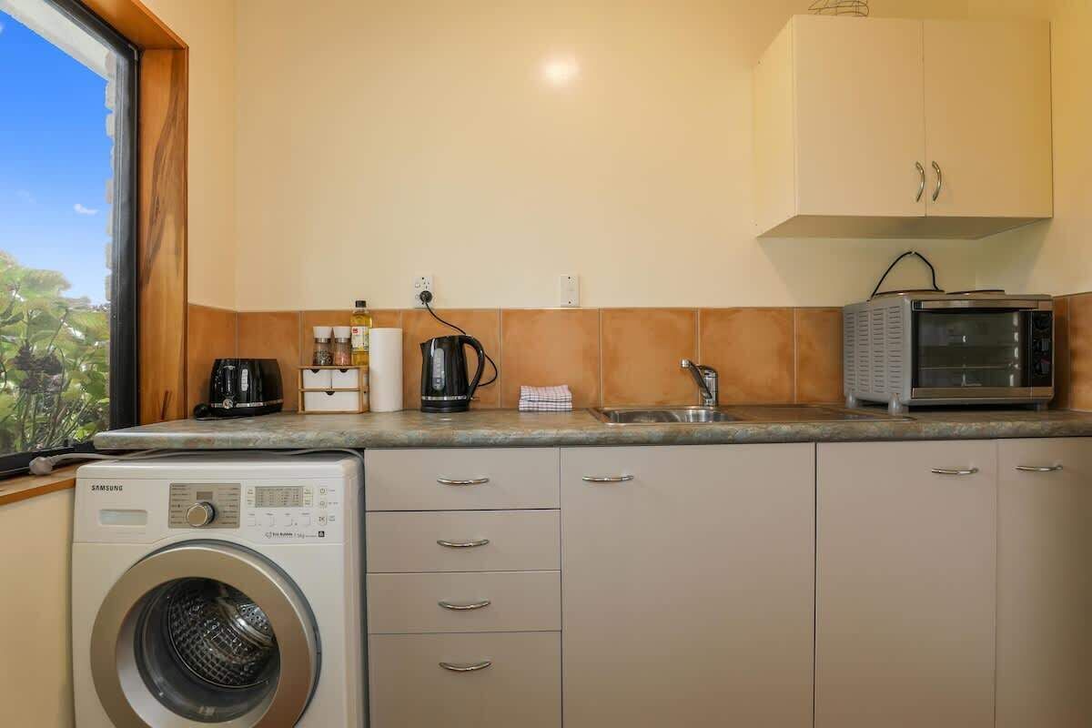 A compact kitchen with a washing machine, a coffee maker, a microwave, and cabinets.