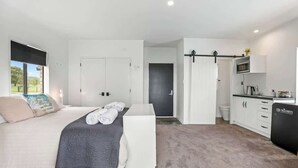 Een slaapkamer met een bed, nachtkastje, bureau, stoel, kledingkast, en een keukenhoek met een magnetron en spoelbak.