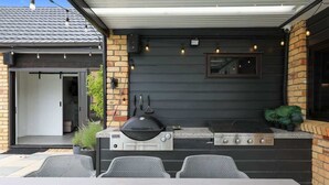 Een buitenkeuken met een barbecue, een inbouwoven en een zithoek met stoelen.