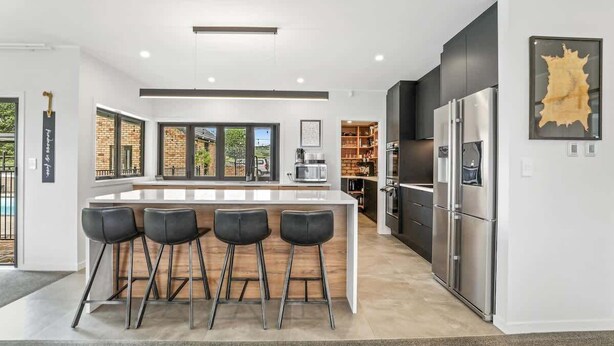 Een moderne keuken met een centraal eiland, barkrukken, een koelkast en een groot raam.