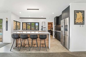 A modern kitchen with a central island, bar stools, a refrigerator, and a large window. - Airport Oasis - Pool, Spa, Games, Sleeps 11 (Rotorua)