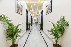 A hallway with potted plants on either side, framed artwork on the walls, and a tiled floor. - FabHotel Golden Leaf - Nr. Medanta Hospital (Gurugram)