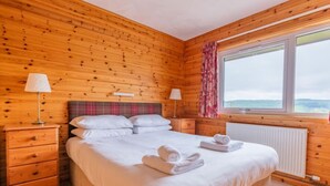 Een houten slaapkamer met een bed, twee nachtkastjes, lampen, een raam met uitzicht en een ruitjes hoofdbord.