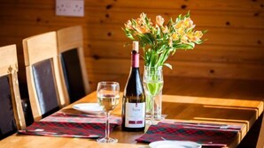 Een houten eettafel met een fles wijn, een glas witte wijn en een vaas met bloemen.