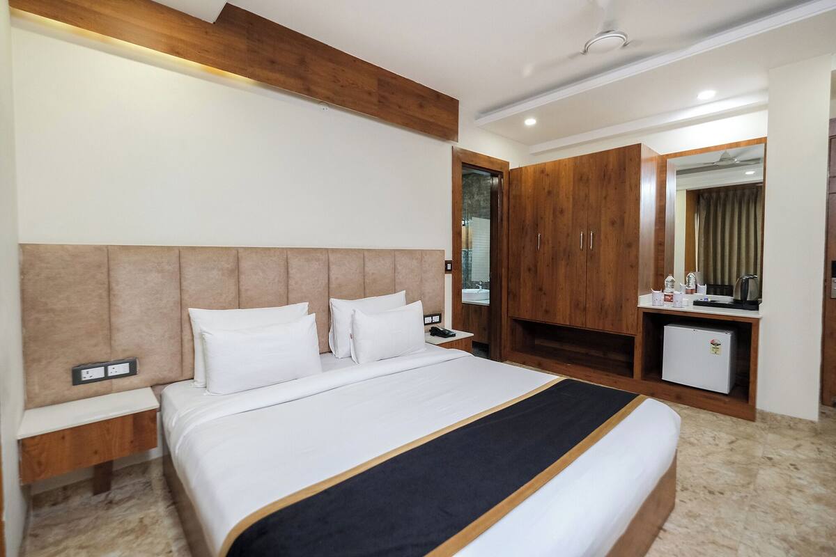 A hotel room with a large bed, wooden headboard, a small kitchenette, and a mirror.