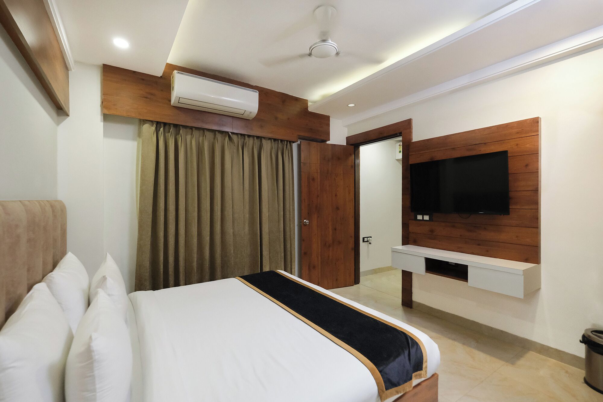 Habitación de hotel con cama, televisor montado en la pared y equipo de aire acondicionado en el techo.