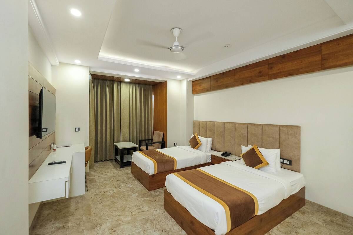 A hotel room with two beds, a desk, a chair, a TV, and a ceiling fan.