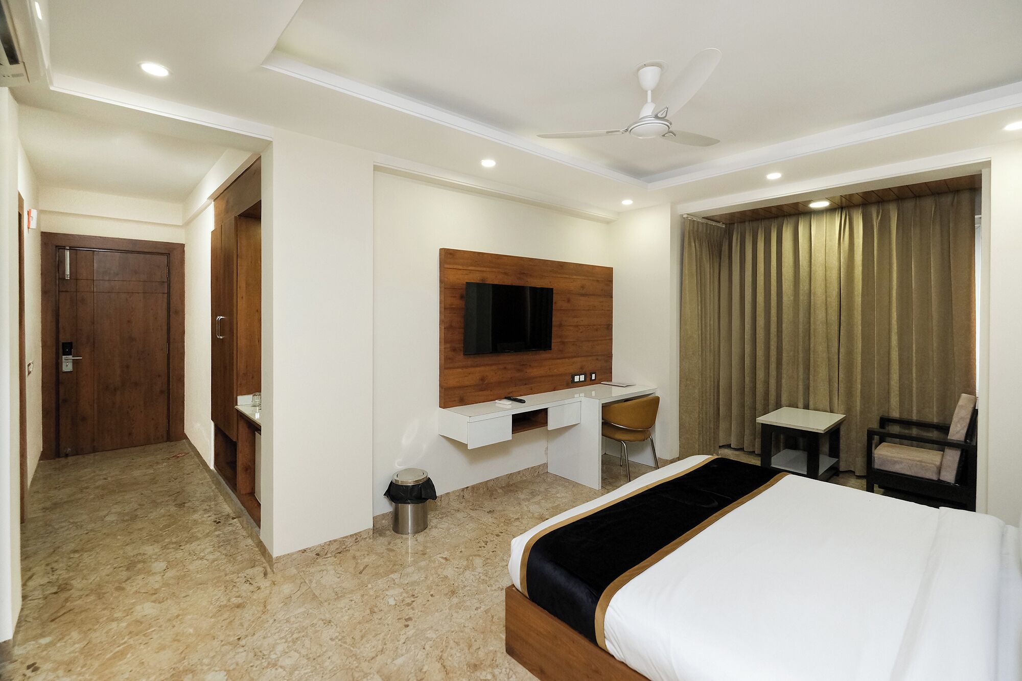 A hotel room with a bed, a desk, a chair, a TV, and a ceiling fan.