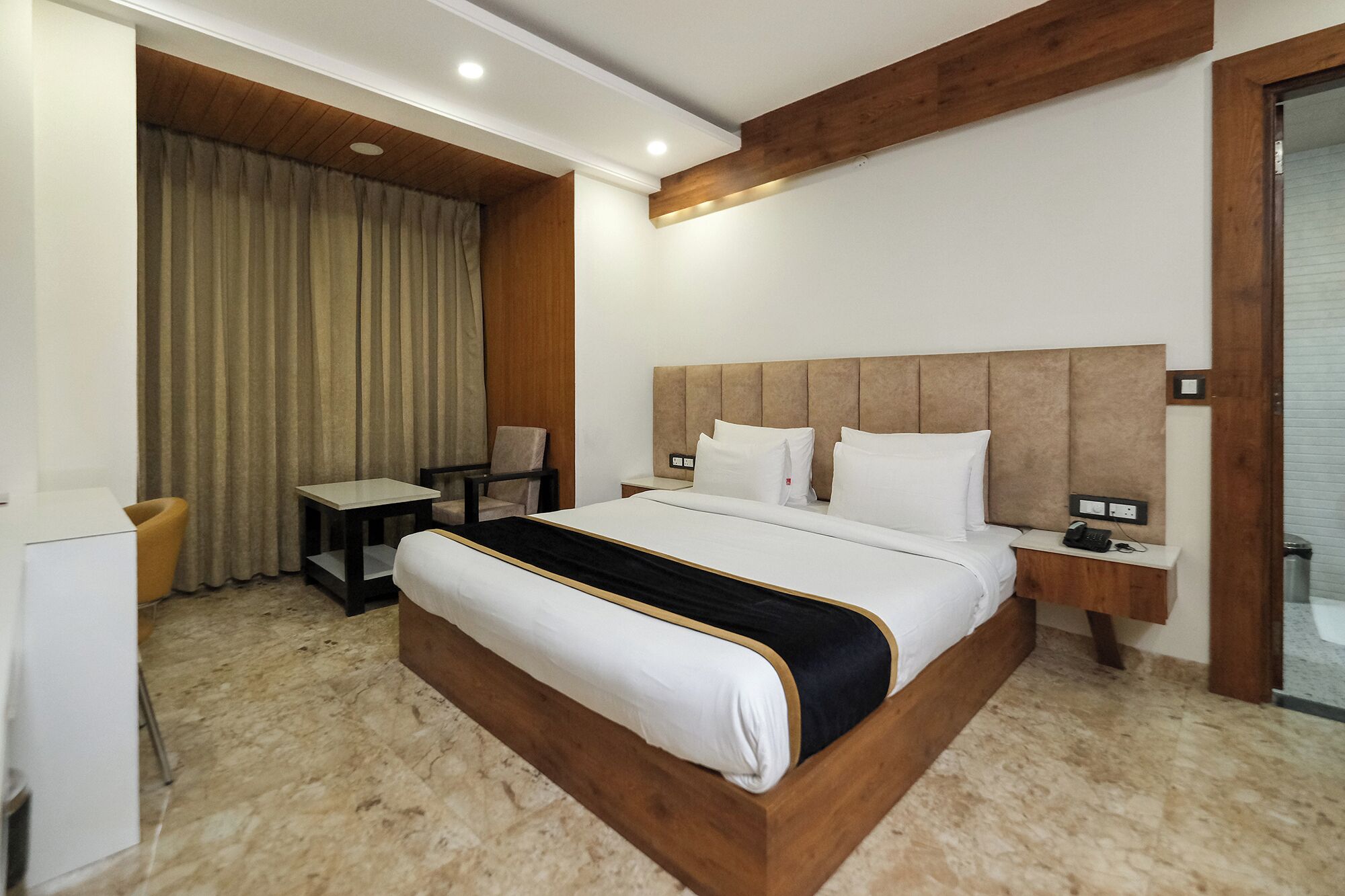 A hotel room with a large bed, a desk, a chair, and a bathroom visible through an open door.
