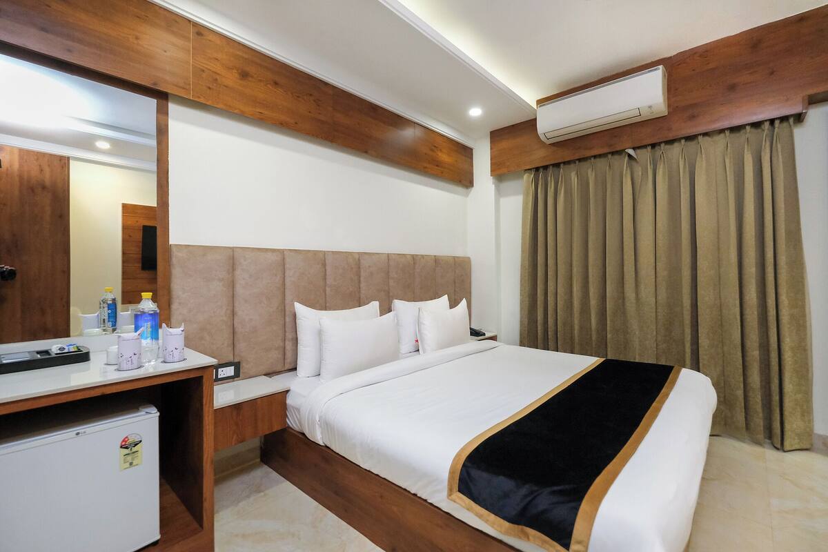 A hotel room with a bed, a desk, a mirror, an air conditioner, and a curtain.