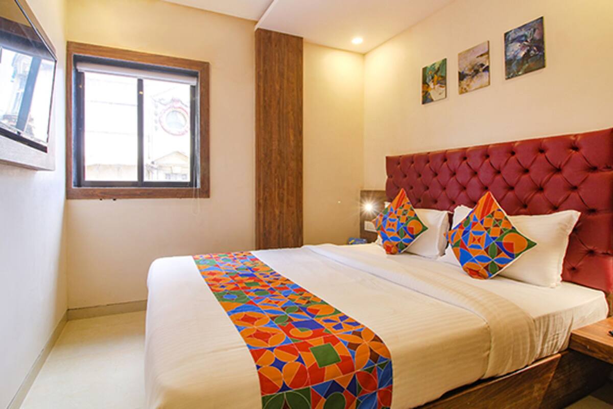 A hotel room with a large bed, a wooden headboard, and a window with blinds.