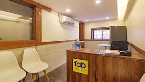 A reception desk with a sign for 'Fab Hotels', two white chairs, a window, and a refrigerator. - FabHotel Peninsula (Mumbai)
