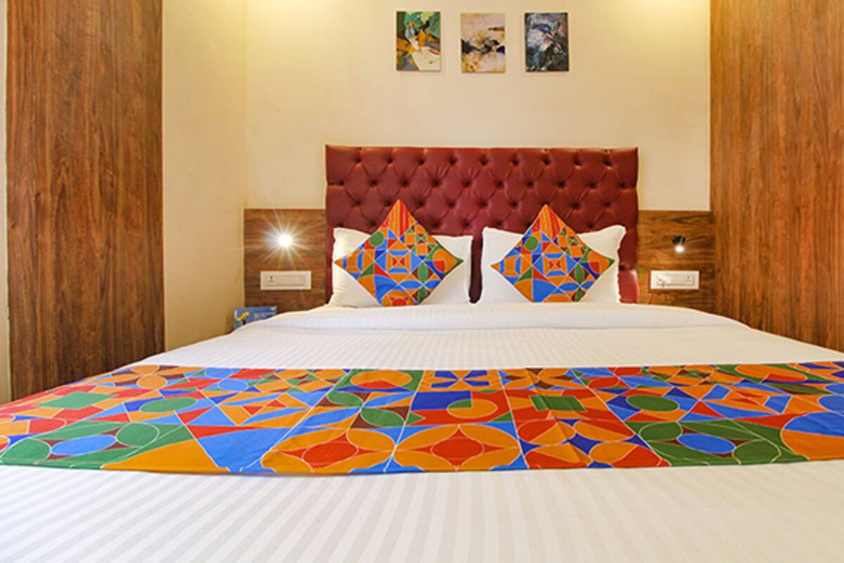 A hotel room with a large bed, a red tufted headboard, two bedside tables with lamps, and colorful geometric-patterned bedding.