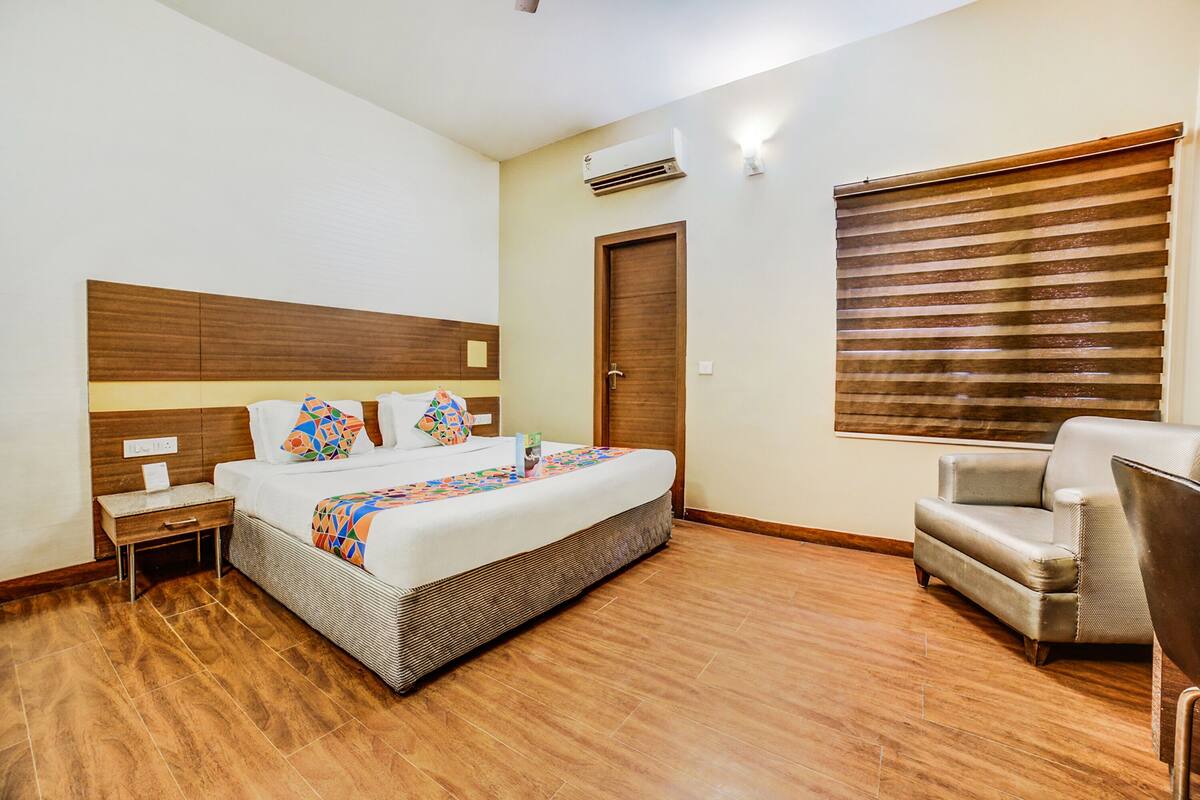 Ein Hotelzimmer mit einem großen Bett, einem Nachttisch, einem Stuhl und einem Fenster mit Jalousien.