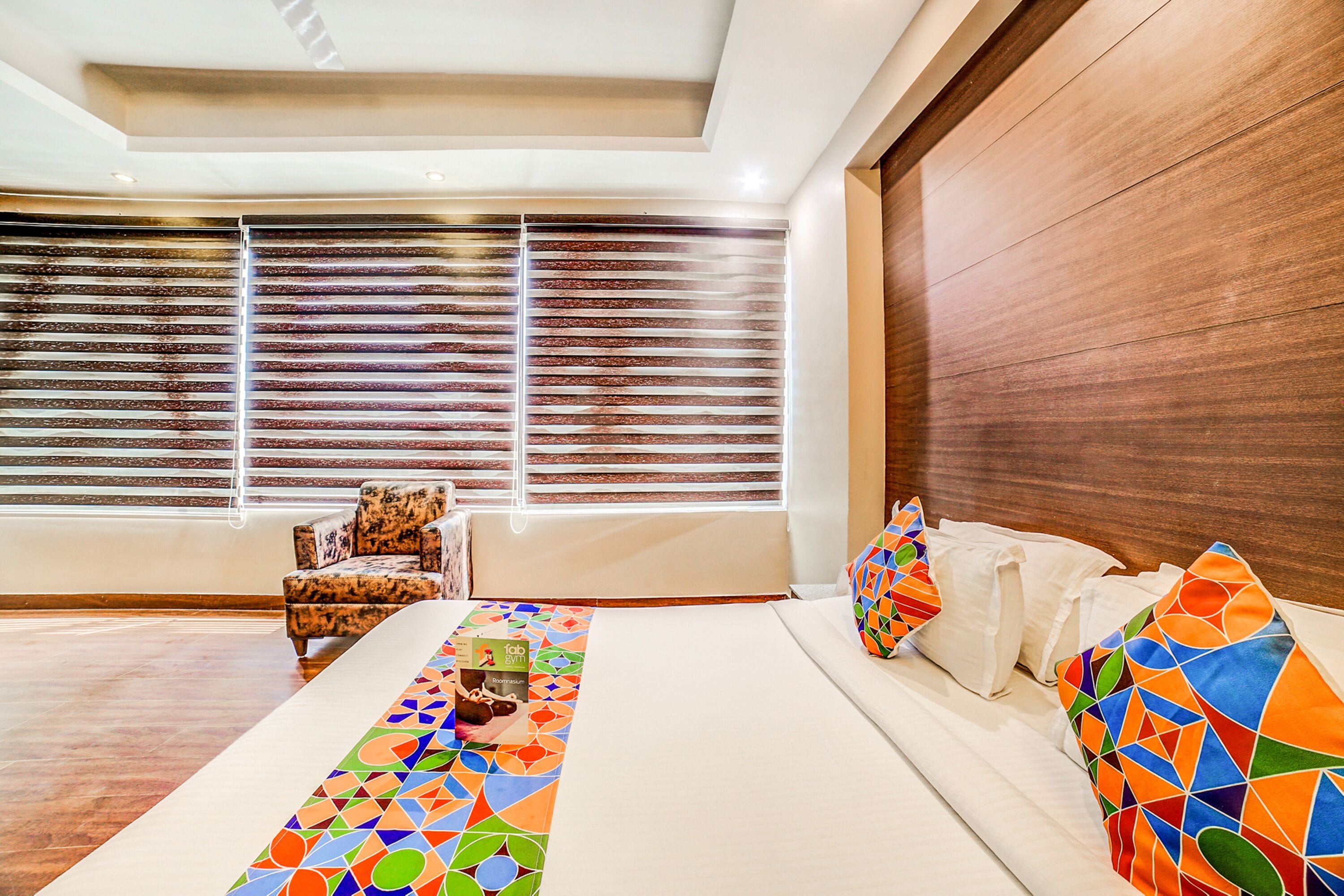 A modern hotel room with a large bed, a sofa, a chair, and a window with blinds.