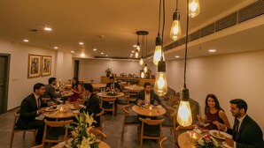 A restaurant with round tables, hanging light fixtures, and framed artwork on the walls.
