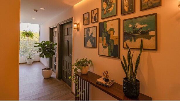 A hallway with wooden flooring, potted plants, and framed artwork on the walls.