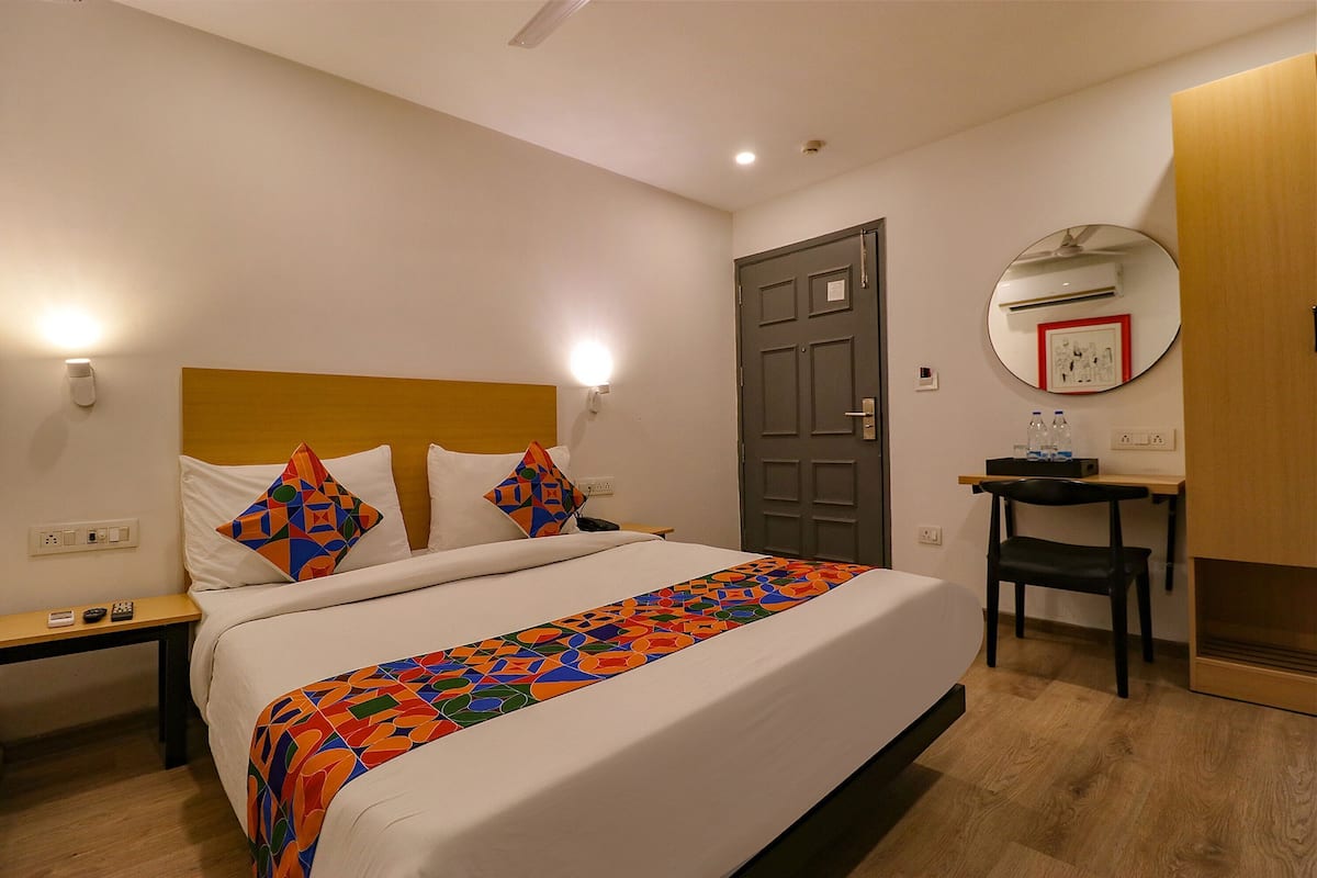 A hotel room with a bed, bedside tables, a desk, a chair, a mirror, and a door.