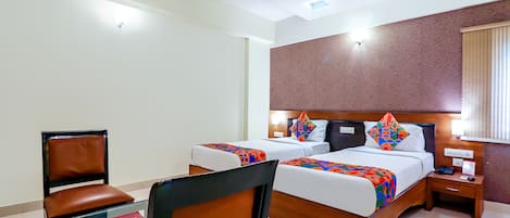 A hotel room with two beds, a desk, a chair, a nightstand, and a ceiling fan.