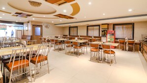 A spacious dining area with multiple tables and chairs, a vending machine, and a large window with blinds. - Fabhotel Nera Regency (Hyderabad)