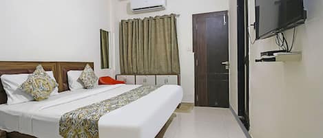 A hotel room with a bed, an air conditioner, a TV, a door, and a curtain.