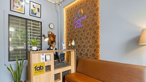 Zona de recepció d'hotel amb un taulell de fusta, una recepcionista, un sofà, una planta en maceta i una paret amb un rètol de làmpades de neó.