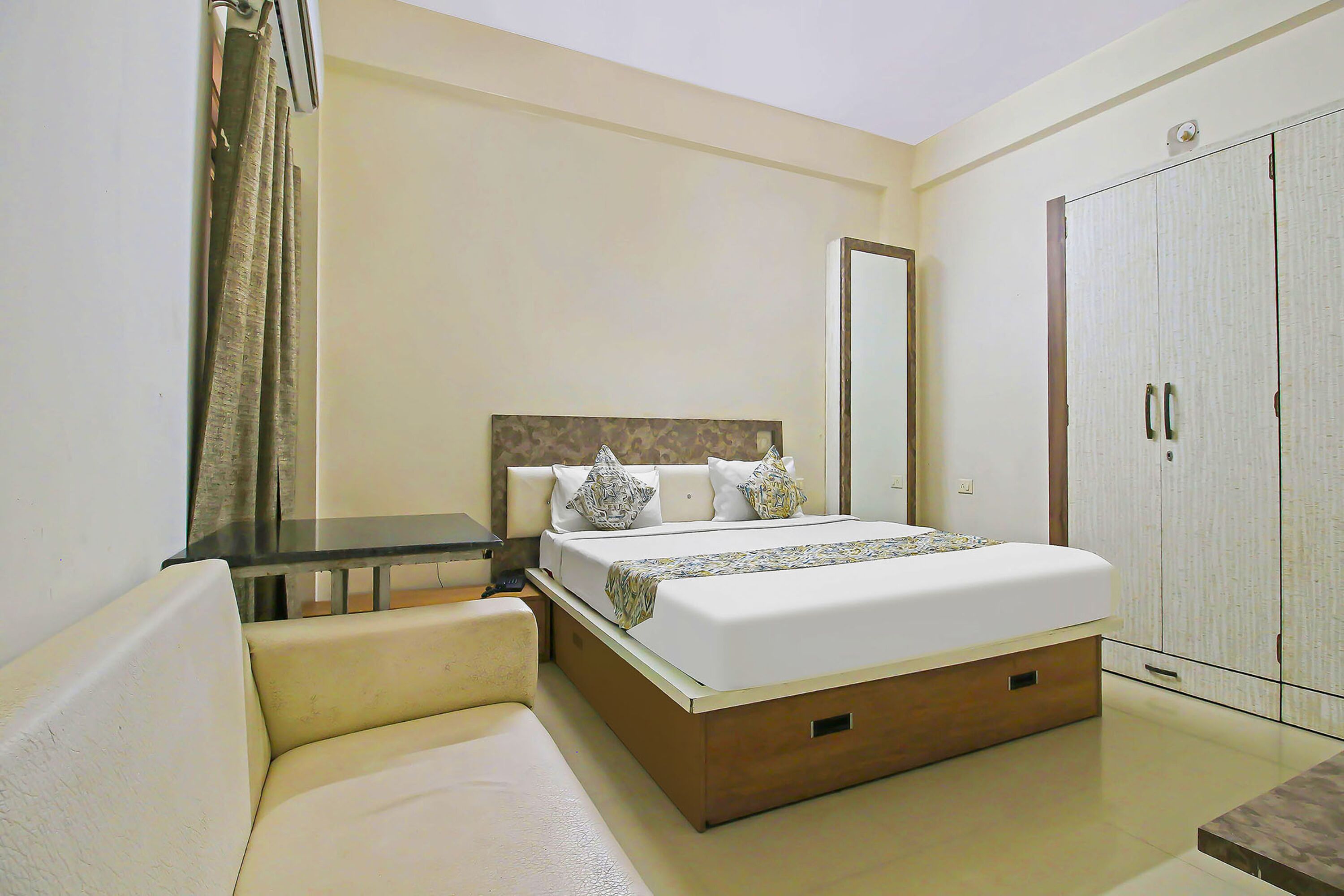 A hotel room with a bed, a bedside table, a wardrobe, and a sofa.