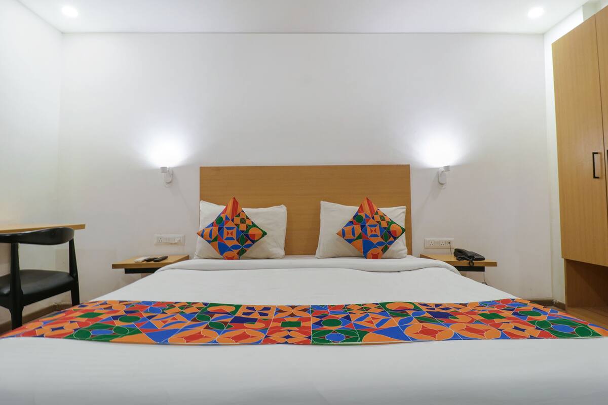 Habitación de hotel con cama, dos almohadas, una mesita de noche, una silla y un aparador con un teléfono.