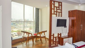 A hotel room with a large window, a bed, a desk with a TV, and a wardrobe. - FabHotel The Golf Inn - Nr Botanical Garden Metro (Noida)