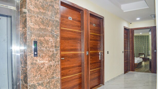 A hotel corridor with marble flooring, wooden double doors with numbers, and a bed visible through an open door. - FabHotel The Golf Inn - Nr Botanical Garden Metro (Noida)