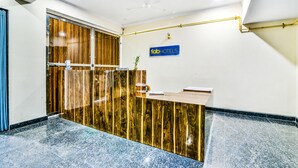 A reception area with a wooden reception desk, a sign reading "fabHOTELS", and a ceiling fan. - Fabhotel Merriment (Noida)