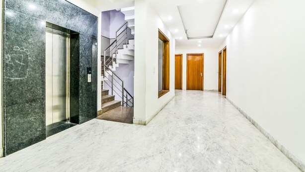 A modern hallway with a marble floor, a staircase, and wooden doors. - Fabhotel Merriment (Noida)