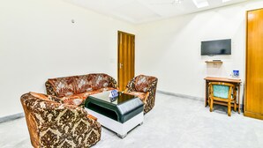A living room with a sofa set, a coffee table, a TV, and a wooden door. - Fabhotel Merriment (Noida)