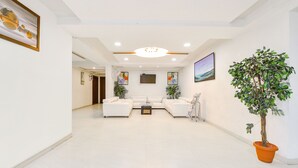 A spacious living area with a white sofa set, a coffee table, and a potted plant. - Fabhotel Skyland (Ahmedabad)