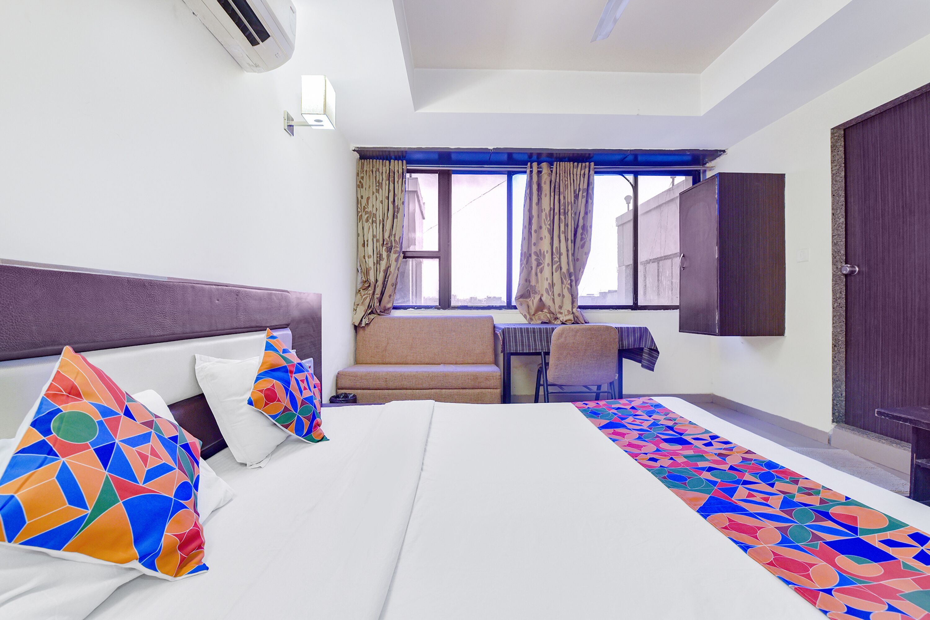 A hotel room with a bed, a sofa, a desk, and a window with curtains.