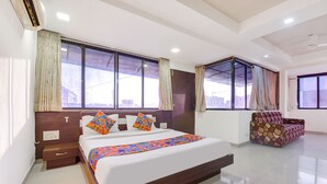 A modern hotel room with a large bed, a nightstand, a chair, and a window with curtains. - Fabhotel Skyland (Ahmedabad)