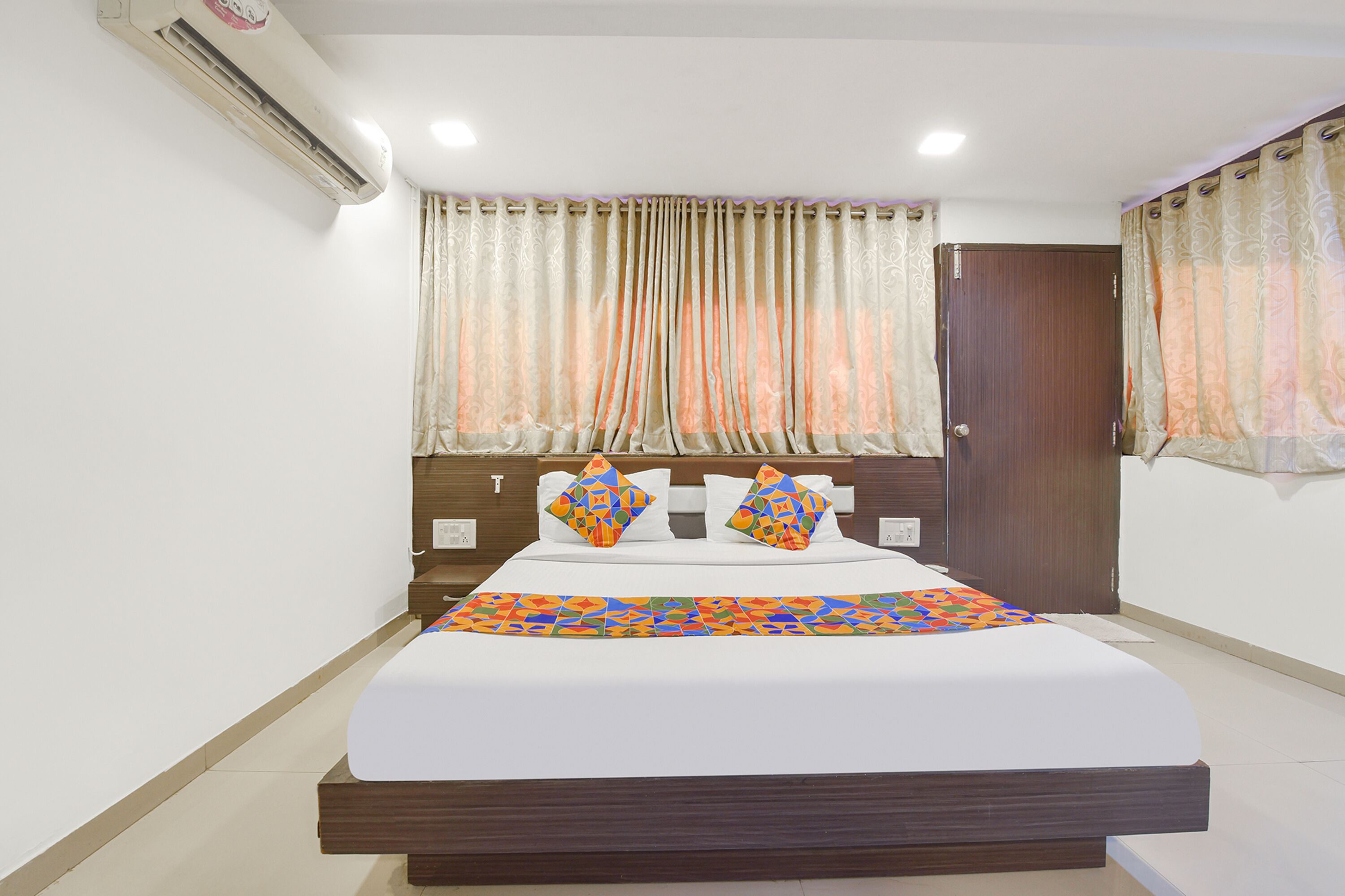 A neatly made bed with a colorful bedspread, two pillows with a geometric pattern, and a wooden headboard.